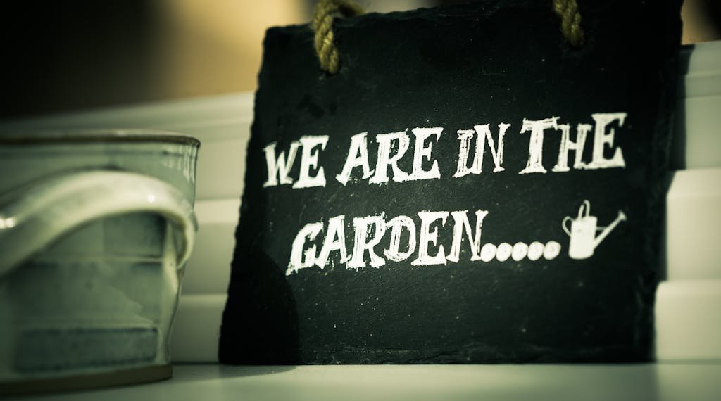 Close-up of a rustic slate sign reading "We Are In The Garden."